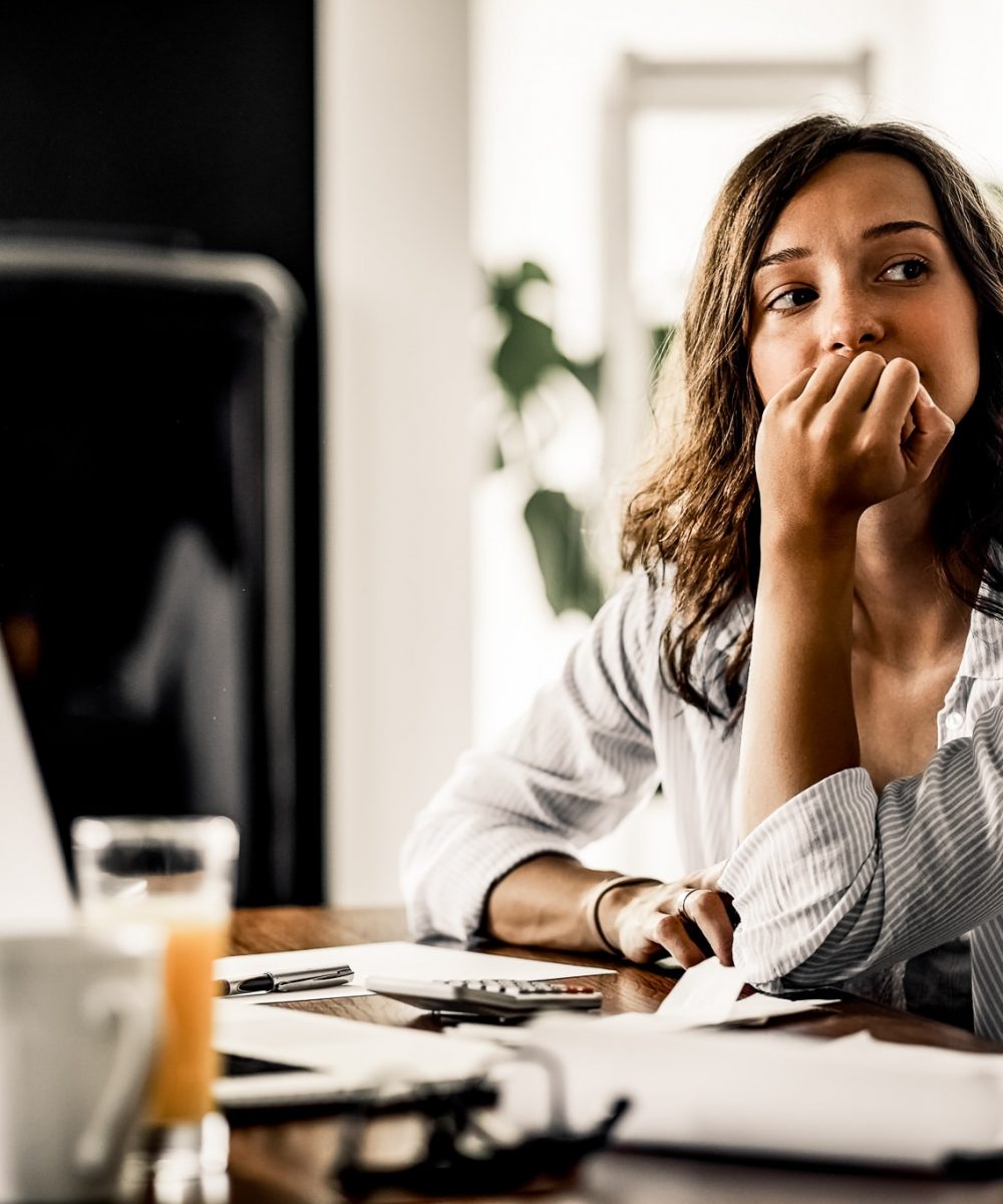 Pensive woman feeling worried while working on home finances. Young worried woman thinking of something while calculating her home budget.